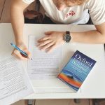 Student writing test using paper and Oxford dictionary on desk in classroom