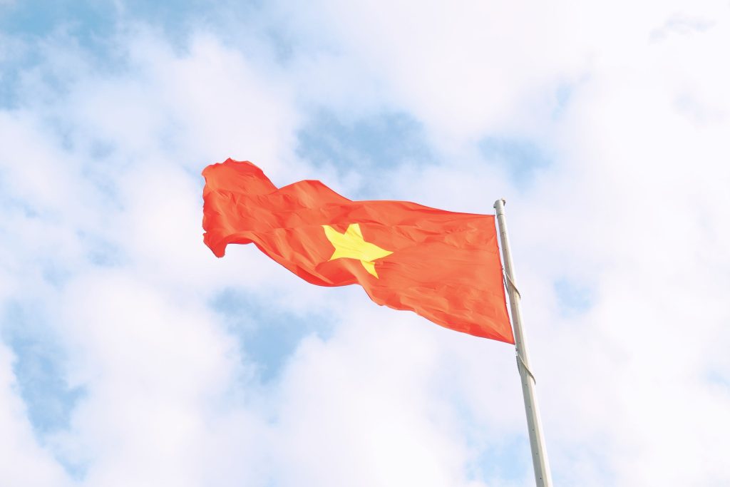 The vibrant red flag of Vietnam with a yellow star waves under a clear blue sky.